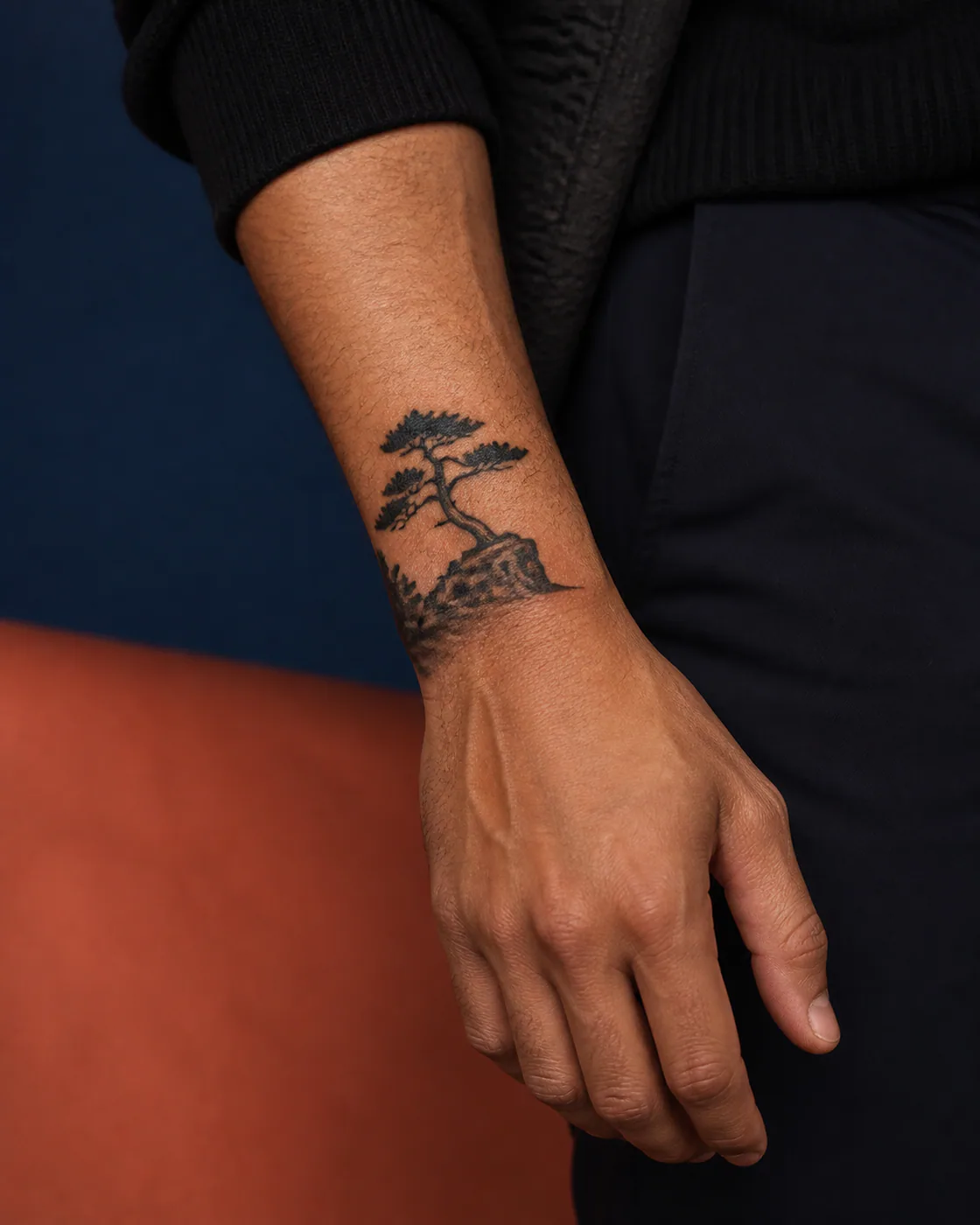 Blackwork tattoo of a windswept pine leaning over a rocky ledge on the wrist