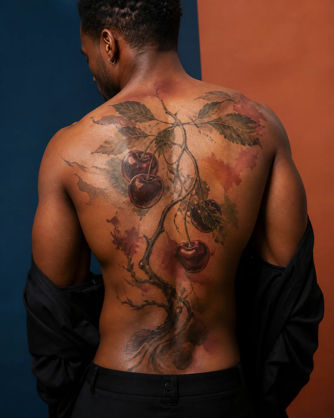 Watercolor tattoo of dark cherries hanging from a twisting leafy branch with a three-part family motif on the full back