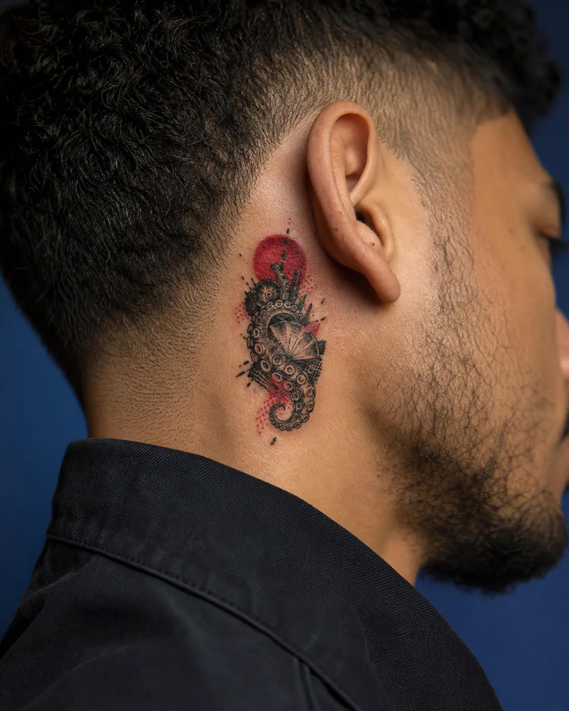 Trash Polka tattoo of an octopus arm curling protectively around a shell on the behind the ear