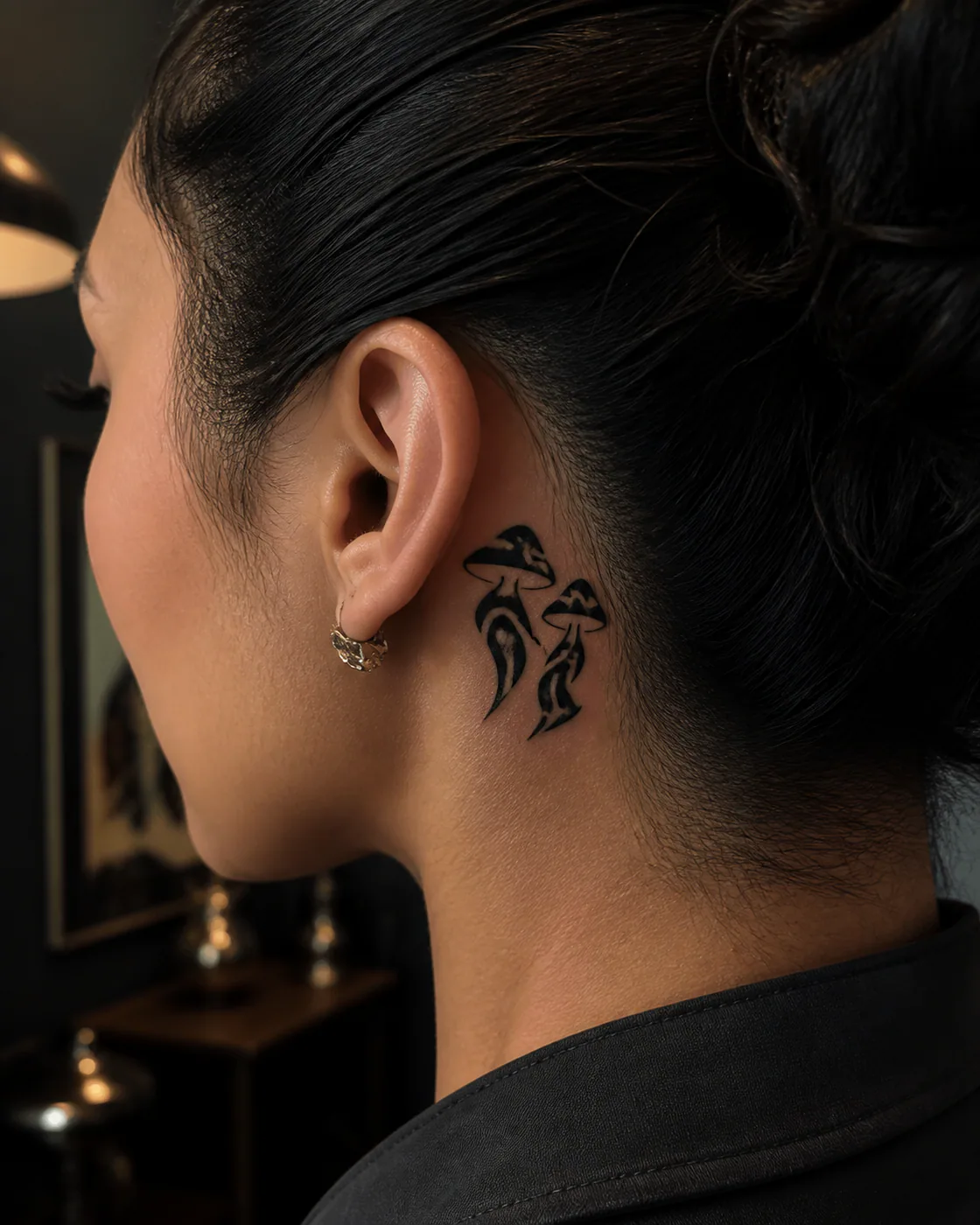 Tribal tattoo of two dancing mushrooms wearing oversized boots on the behind the ear