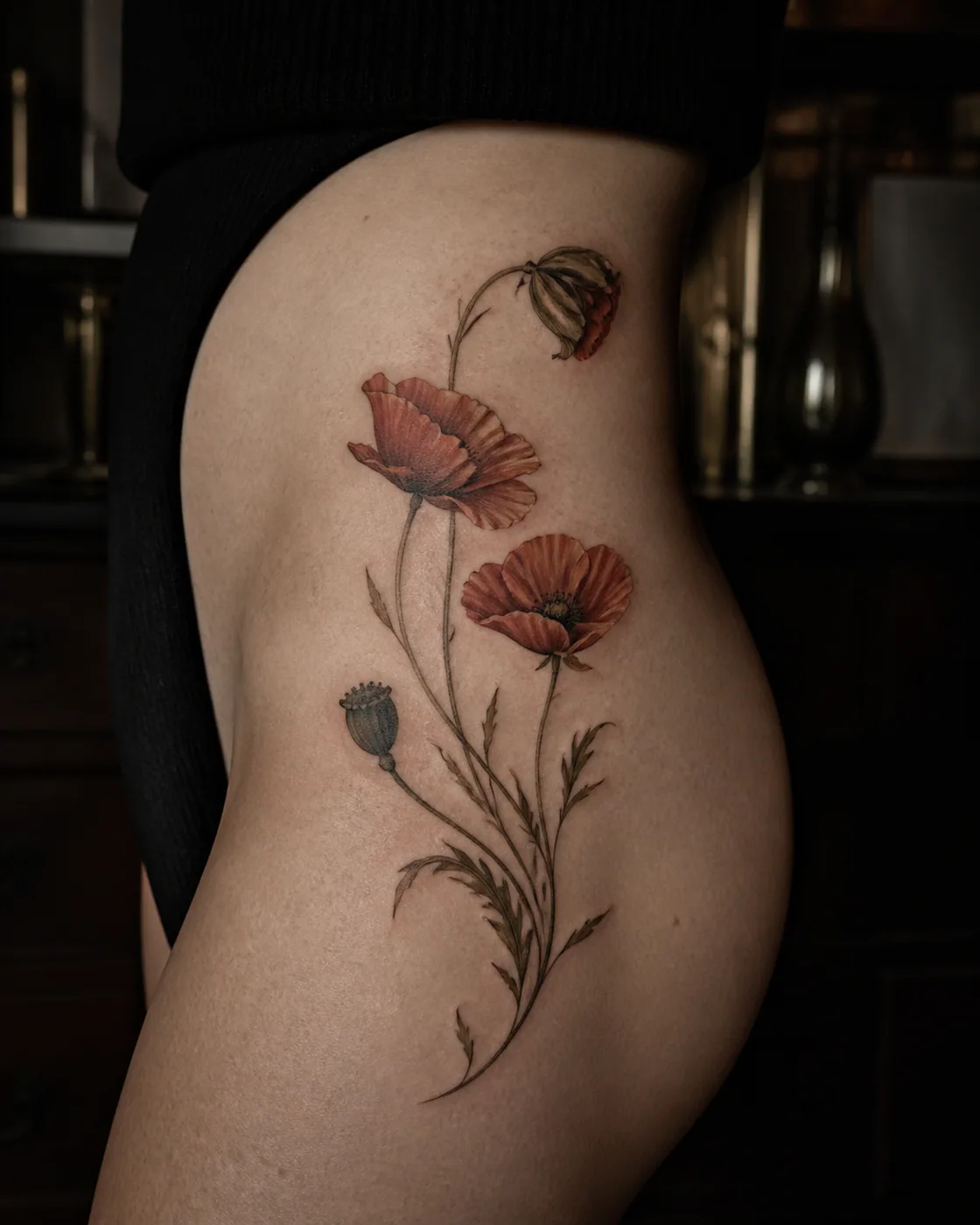 Floral tattoo of three wind-bent poppies at different stages of bloom on the hip