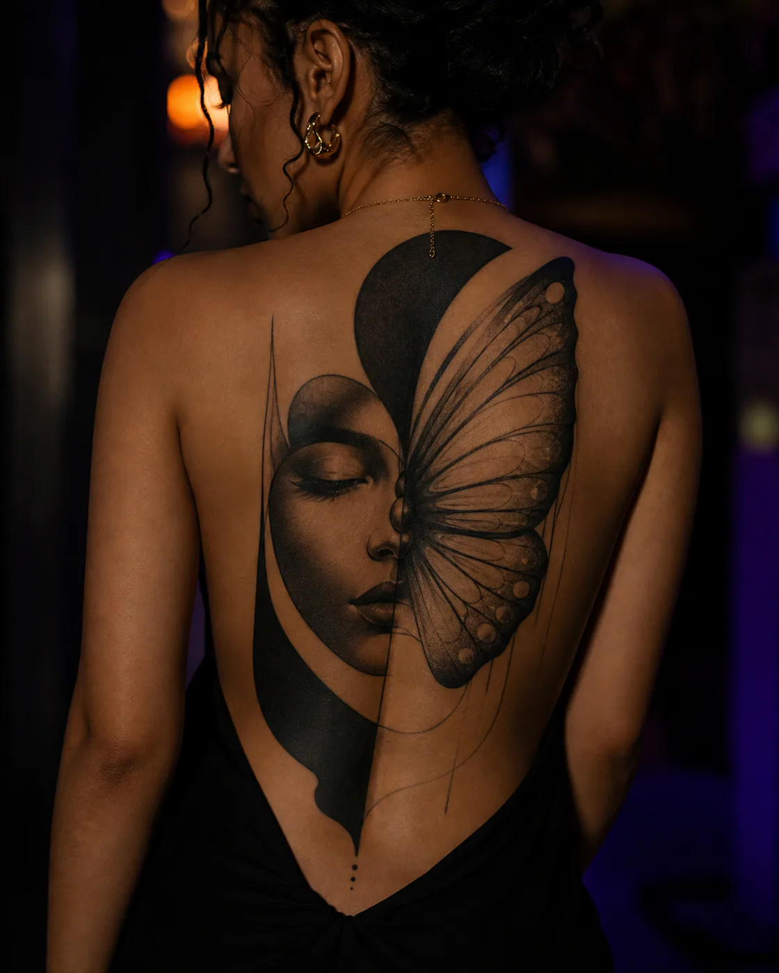 Blackwork tattoo of a quiet face half concealed by a translucent moth wing on the full back