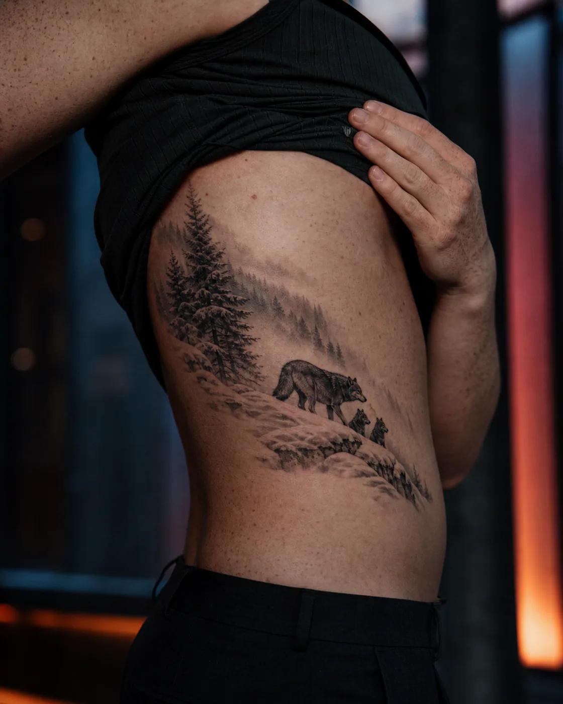 Realism tattoo of a wolf crossing a snow-softened pine ridge with a three-part family motif on the side ribs