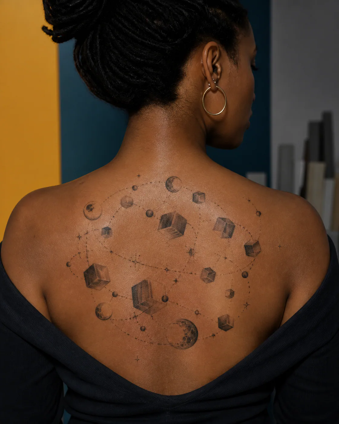 Surrealism tattoo of a loose orbit of dice-like cubes without markings and tiny moons on the upper back