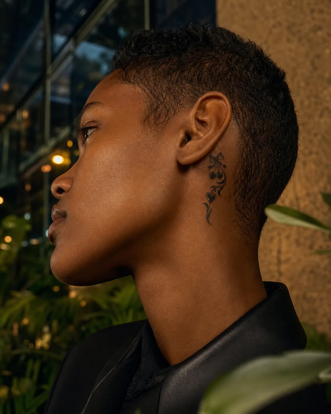 Tribal tattoo of small bows, cherries, leaves, and faceted heart forms on the behind the ear