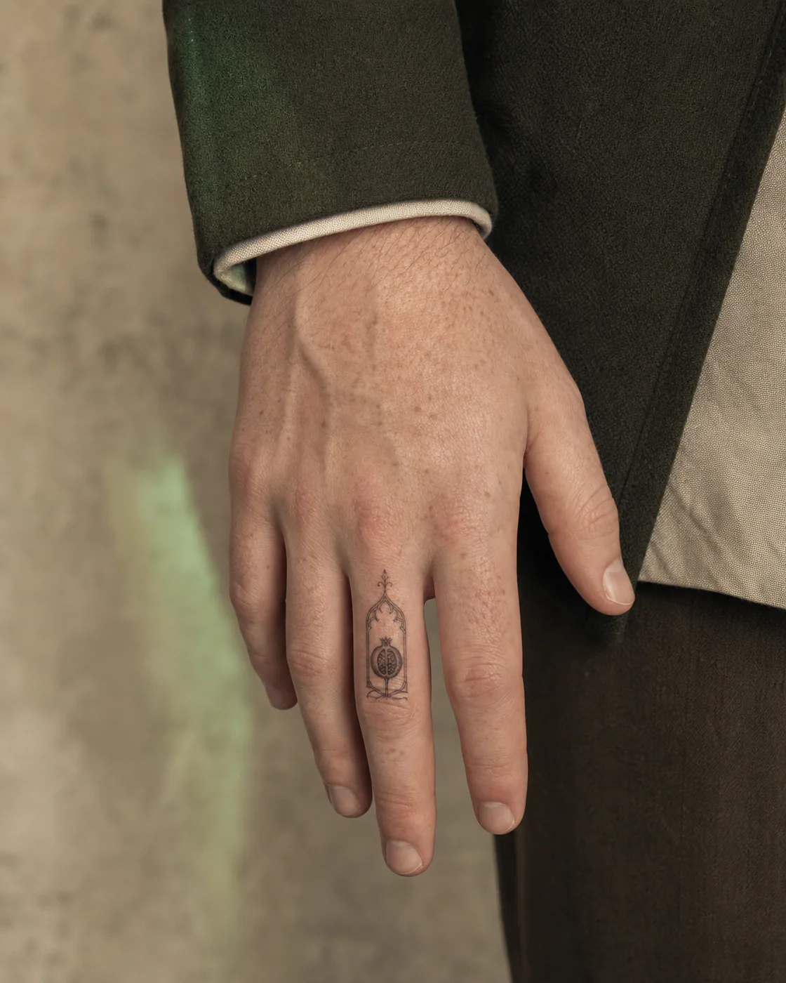 Fine Line tattoo of a reliquary window containing a dried pomegranate on the finger
