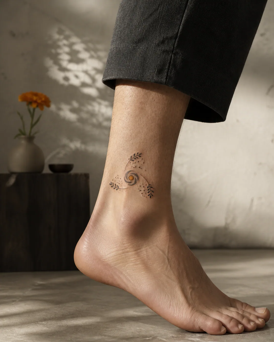 Surrealism tattoo of three groups of tiny leaves and sparks orbiting one central charm with a three-part family connection motif on the ankle