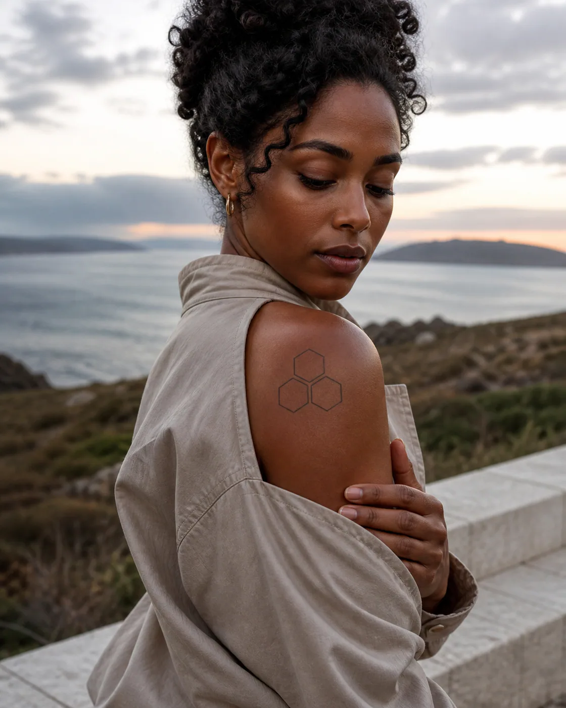 Minimalist tattoo of three geometric cells sharing one precise open center with a three-part family connection motif on the shoulder cap
