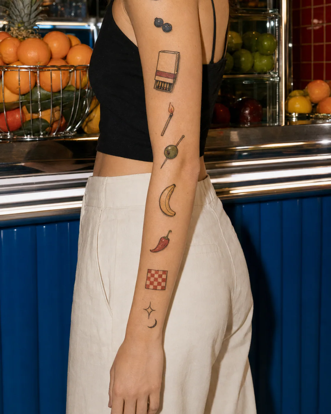 Minimal patchwork sleeve tattoo with a pear, sardine tin, plain matchbook, espresso cup, chili pepper, and tiny heart on light skin