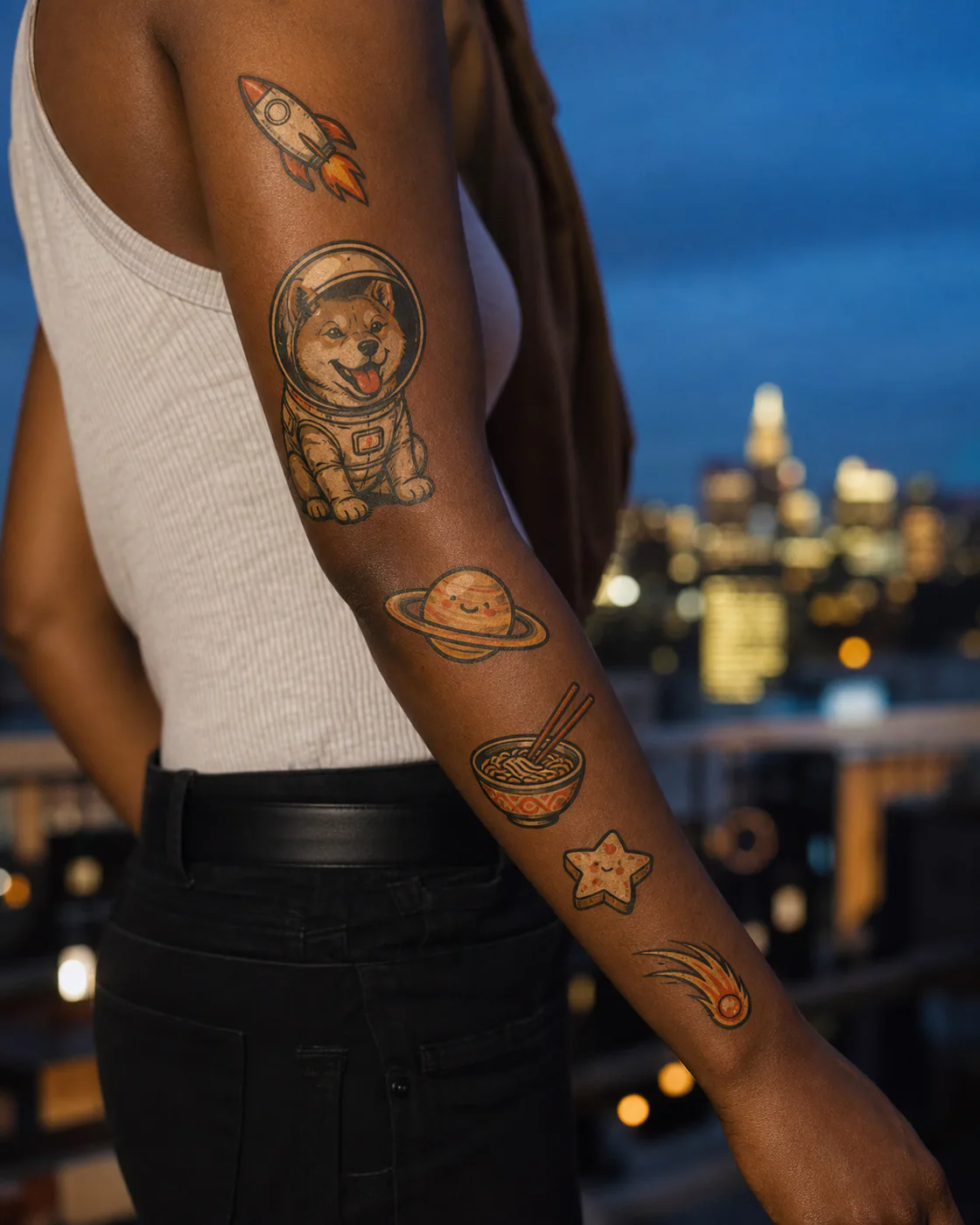 Playful patchwork sleeve tattoo with a helmeted dog, tiny rocket, smiling planet, floating noodle bowl, star cookie, and comet on deep skin