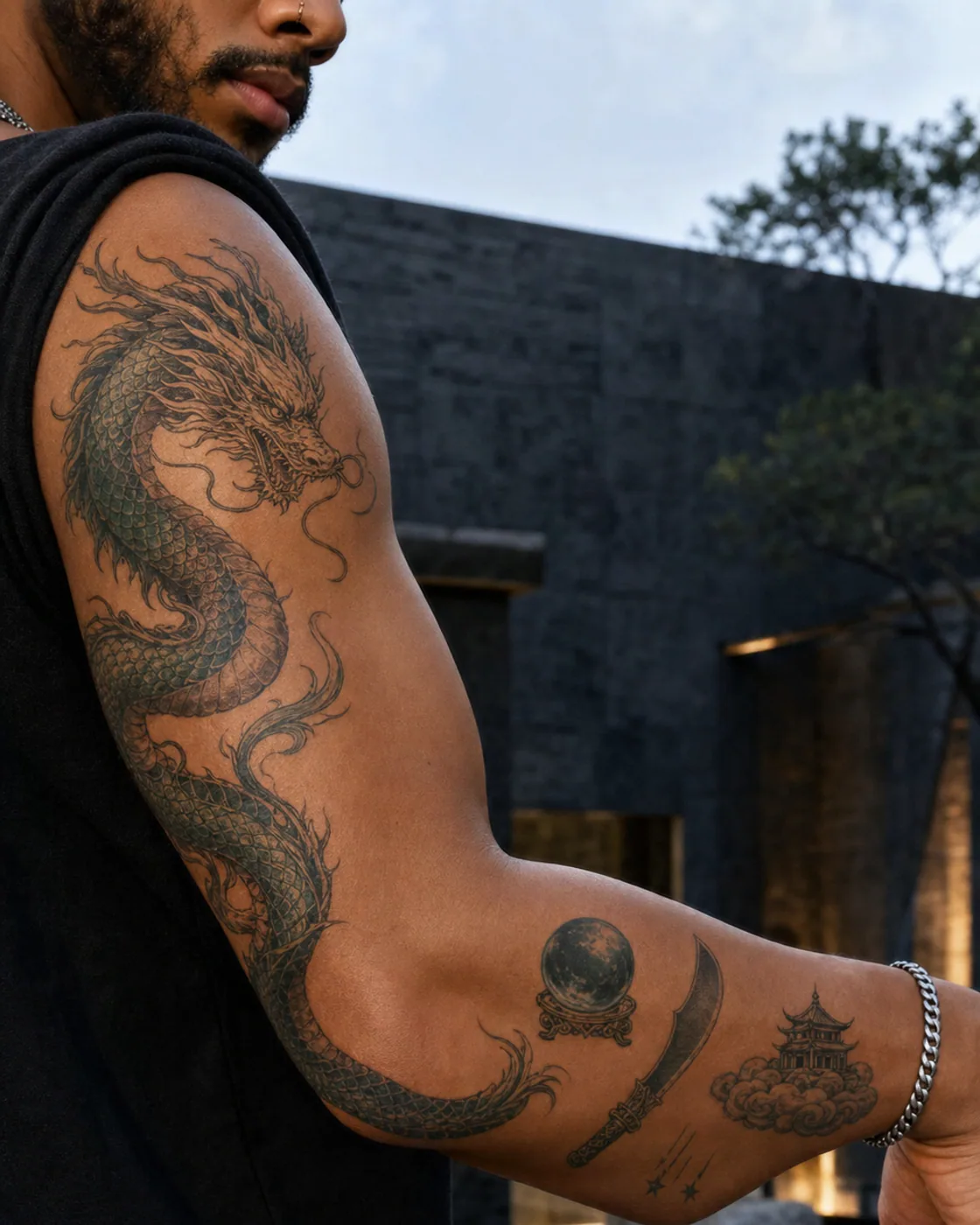 Bent-arm illustrative patchwork sleeve tattoo with a coiled dragon, oracle sphere, crescent blade, cloud temple, and falling stars on brown skin