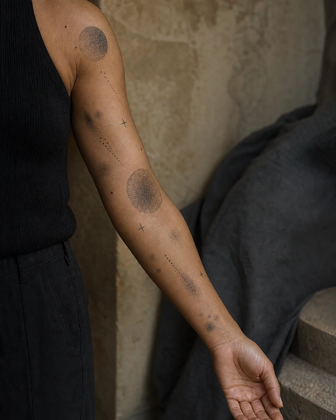 Dotwork patchwork sleeve tattoo on medium skin with stippled circles, soft halos, tiny crosses, tapered dot trails, and clear breathing room between anchor pieces